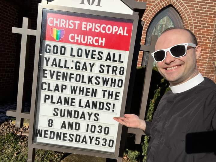 Father Ryan stands next to the church sign that reads "God Loves All Y'll: Gay, Straight, even folks who clap when the plane lands!" Sundays at 8am and 10:30am along with Wednesdays at 5:30pm.